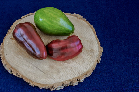 Red bell peppers and avocado on wooden board.