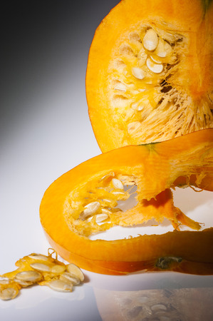 In the foreground on slice of orange pumpkin  We can see also pulp and seeds  In the background the cutting pumpkin with front longitudinal section  Freshly harvest in autumn before shooting on studio  Background with reflections in gray gradation の写真素材