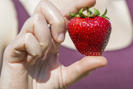 Selective focus on a big specimen of strawberry with heart shaped holding by a womanの写真素材