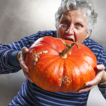 Halloween theme. Closeup of an old woman eating a big ripe pumpkin freshly harvest in autumn. Studio shoot and color image.の写真素材