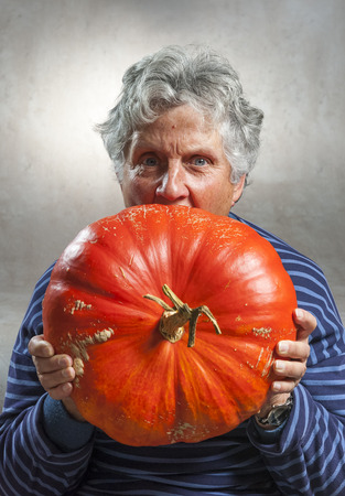 Halloween theme. Closeup of an old woman eating a big orange pumpkin freshly harvest in autumn. Studio shoot and color image.の写真素材