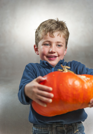 Portrait of little boy holding a big orange pumpkin. Halloween theme. Studio shoot after freshly harvest in autumn. Color imageの写真素材