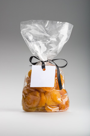 Tasty candied apricots into elegant transparent plastic bag with luxury black ribbon isolated on grey background. Shooting in studio.の写真素材
