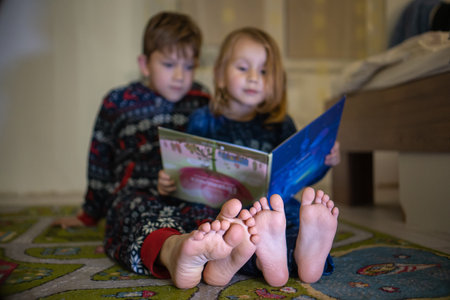 Brother and sister read book in pyjamas bare feet evening sleep family