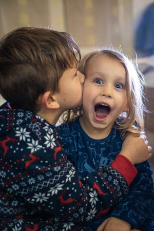 Two siblings in pajamas, sister kiss brother, funny emotionsの写真素材