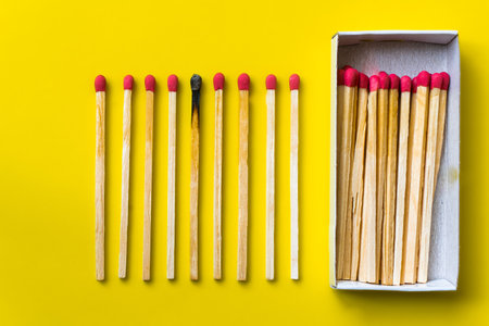 Success, defeat, achievement. The concept of happiness. Matches on yellow background. Burnt dark match among normal matches. Burning match fire to its neighbors, a metaphor for ideas and inspirationの写真素材