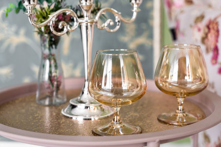 Old style retro candles and wine glass on a tray, vintage home decor on an a table, in light tones
