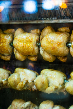 Close-up shot of a steamy rotisserie machine window with water drops. Grilled roasted whole chickens with tasty golden-yellow roasted skin on a turning spit in a row. Restaurant, butcher shop roaster.の写真素材