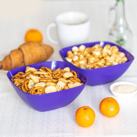 Two blue bowls of snacks and cookies on stone table. Nuts, chips, nachos, crackers.の写真素材