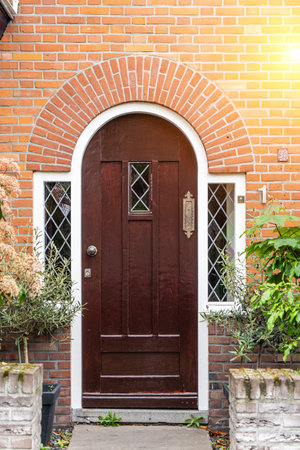 Wooden front door of a home. Front view of a wooden front door on a brick house with windows plants and a wide view of the porch and front walkway. horizontal shot.の写真素材