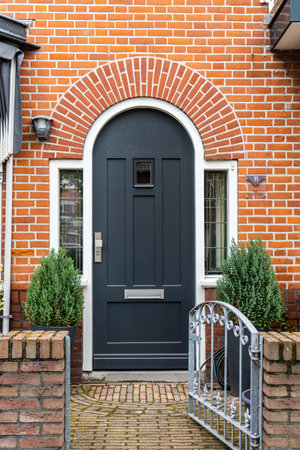 Wooden front door of a home. Front view of a wooden front door on a brick house with windows plants and a wide view of the porch and front walkway. horizontal shot.の写真素材