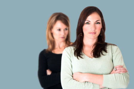 Confident young brunette with arms crossed and her jealous opponent in the backgroundの写真素材