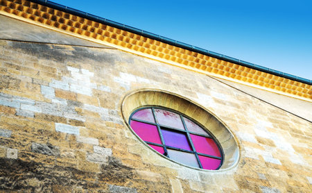 Wall of a chapel in France, with a round stained glass window against blue skyの写真素材