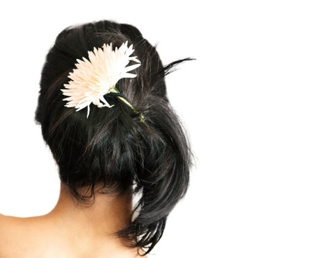 Back of a young woman with a flower in her black hairの写真素材