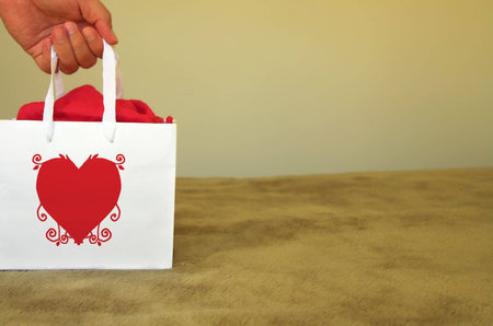 man holding a white paper gift bag with a heart design on it の写真素材