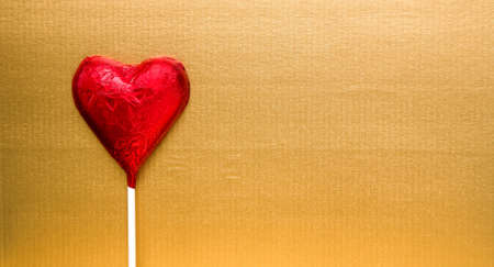 Red heart shape chocolate on lolly stick and golden paper background with copy spaceの写真素材