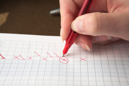 Woman teacher marking a test paper with crosses and check marks, shallow depth of filed focus on X