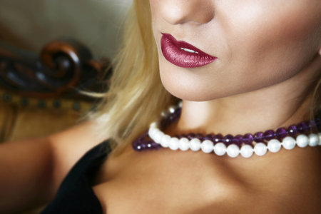 Young beautiful blond with full red lips and soft smile, sitting, white and purple beads on her neckの写真素材
