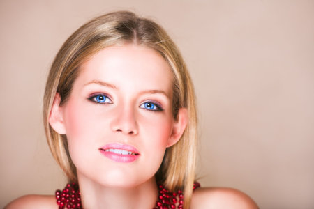 Blond teenage girl with loose straight hair on beige background with red shiny necklace and soft smile. Natural make-up,  has skin texture.の写真素材