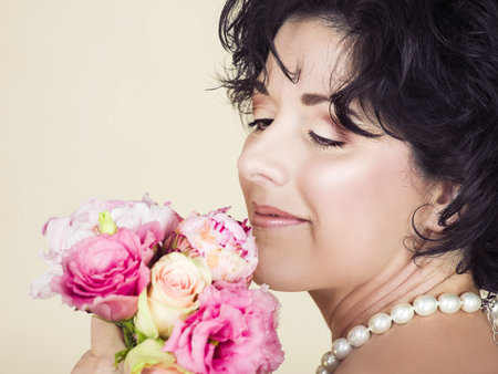 Beautiful adult woman  with black curly hair holding pink spring flowers bouquet. Good visible skin texture with pores and fine wrinklesの写真素材