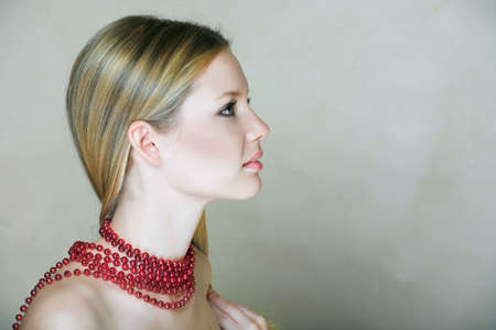 Beautiful young woman with natural make-up and long blonde hair, with red shiny beads in low-key pastel effect on texture background の写真素材