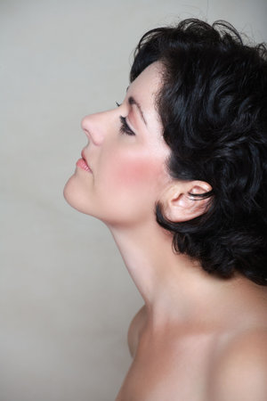 Beautiful woman in her early 40s late 30s with short curly black hair, in profile. Visible clear skin texture with pores and fine lines appropriate to her age, natural make-upの写真素材