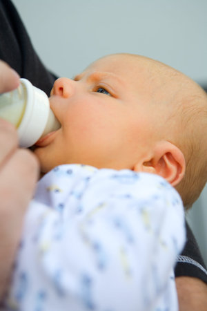 Little baby drinking milk out of bottle held by his parent. Shallow DOF focus on baby eyes