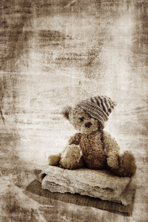 Grunge background with fur teddy bear in handmade hat, sitting on quilts and space for text.の写真素材