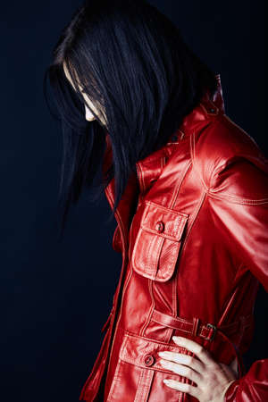 beautiful young woman with dark hair in structured bob wearing a red leather jacket on dark studio background.の写真素材