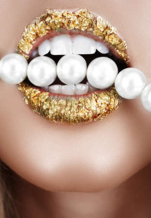 Woman open mouth with gold leaf make-up and teeth biting on faux pearls.の写真素材