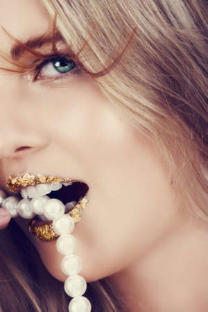 beautiful woman with gold leaf on her lips biting pearl necklace.の写真素材