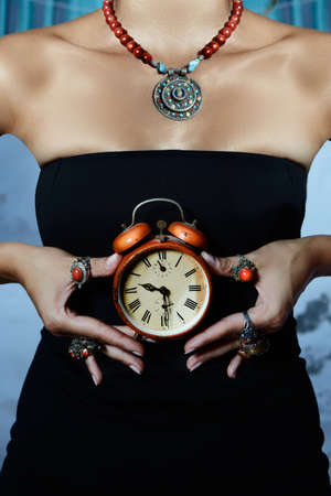 woman wearing black dress and many coral rings holds a red vintage alarm clock の写真素材