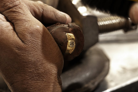 hardworking Goldsmith working on an unfinished 22 carat gold ring with his aged handsの写真素材