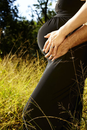 young 8 months married pregnant couple outdoors in green sunlight grass.