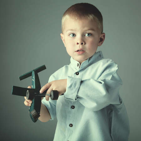 young 3 year old boy wearing blue shirt playing with wooden toy airplane in his hand on blue studio background の写真素材