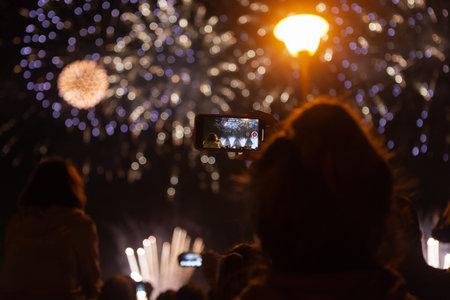 young girl takes fireworks on the phone. people shoot fireworks on the phone. Crowd watching fireworks and celebrating.の写真素材