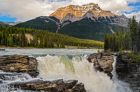 Summer landscape in the mountains with snow-capped peaks, stormy water falling from waterfalls, blue sky with white cloudsの写真素材