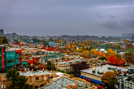 Top view of a modern beautiful city with red, yellow and green trees, a river, a bridge, high-rise buildings and ships, roofs of houses, blue clouds, leaden skyのeditorial素材