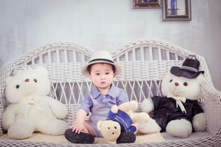 Cute asian baby boy sitting on wicker chair with toy bear