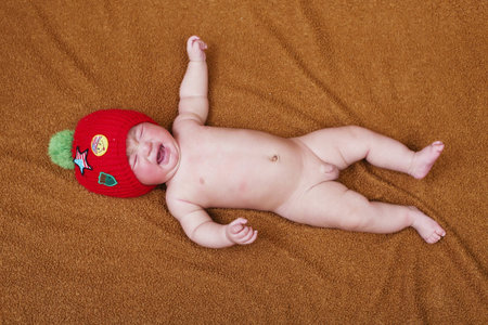 Newborn baby boy in a red hat on a brown background.