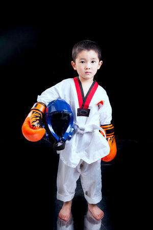 Little boy in white kimono and helmet with boxing gloves on black backgroundの写真素材