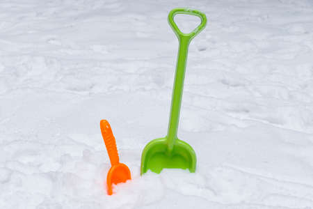 Green and orange children's plastic shovel in the snow. Shovels in the snow.の写真素材