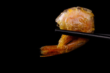 Roasted shrimp hold black chopsticks on a black background. Copy space.
