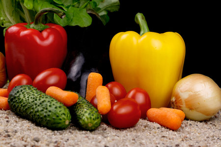 Composition of various juicy vegetables on the sand and black background.