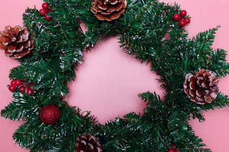 Christmas wreath with red balls, berries and pine cones on a pink background. Christmas decor. Copy...