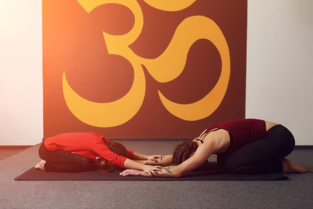 Mother and child yoga practice on the background of the Indian symbol of OM. Beautiful young mother with little daughter doing yoga. Sports familyの写真素材