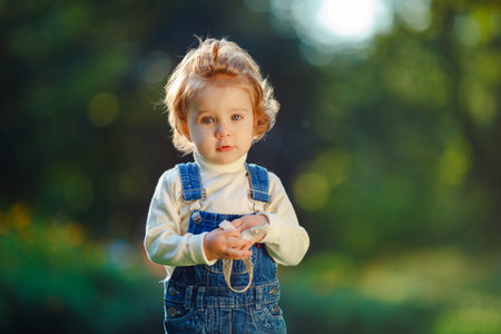 Portrait of a little girl with wavy hair against a background of greenery. The child looks in the picture.の写真素材