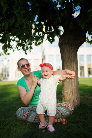 Baby on the grass on a background of sitting momの写真素材