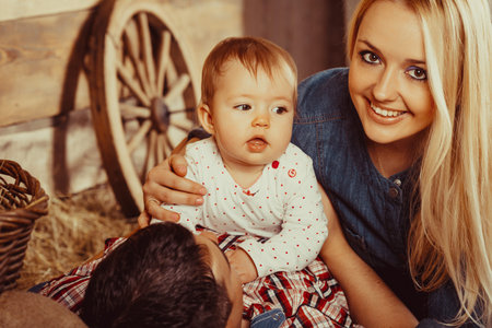 Happy village family, mom and dad playing with a small child lying on the hayの写真素材