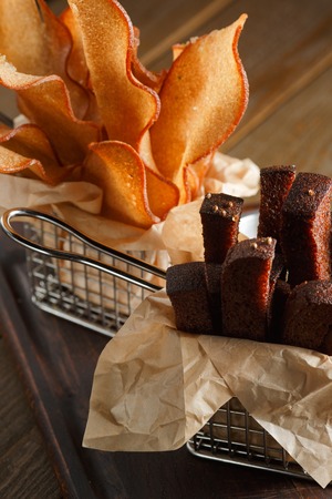 Appetizing fried golden brown croutons of rye and wheat bread in a metal basket on a brown wooden background, backlit, close-upの写真素材
